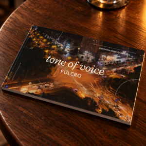 Il manuale del tono di voce di Fulcro su un tavolino in legno di un bistrot, accanto a un bicchiere