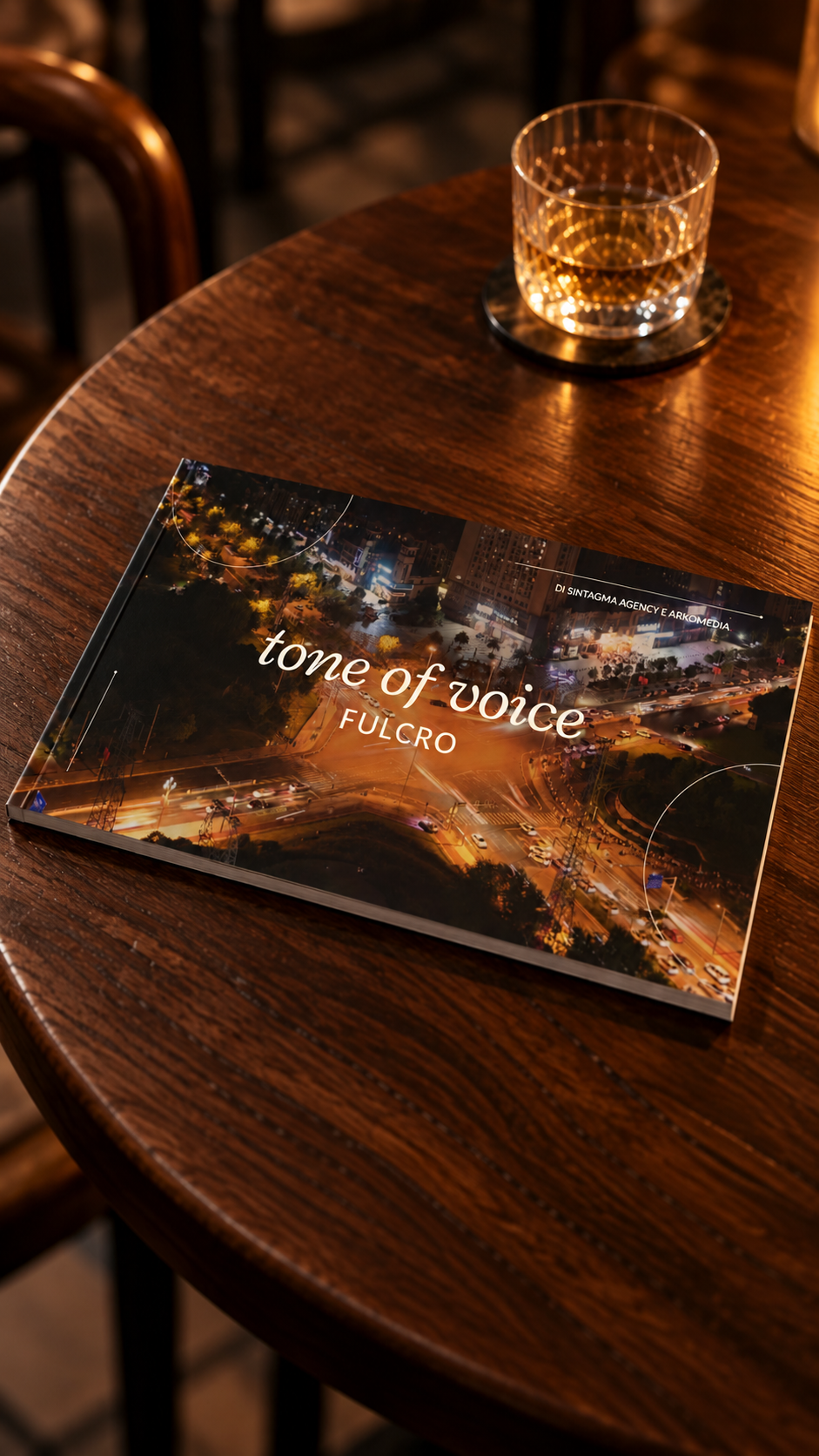 Il manuale del tono di voce di Fulcro su un tavolino in legno di un bistrot, accanto a un bicchiere